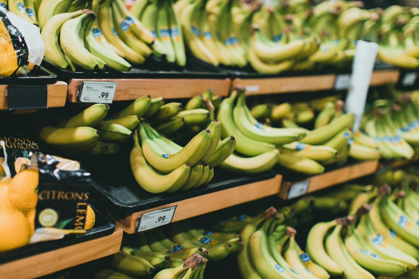 Close-up of fresh bananas stacked on grocery store shelves with price tags visible.