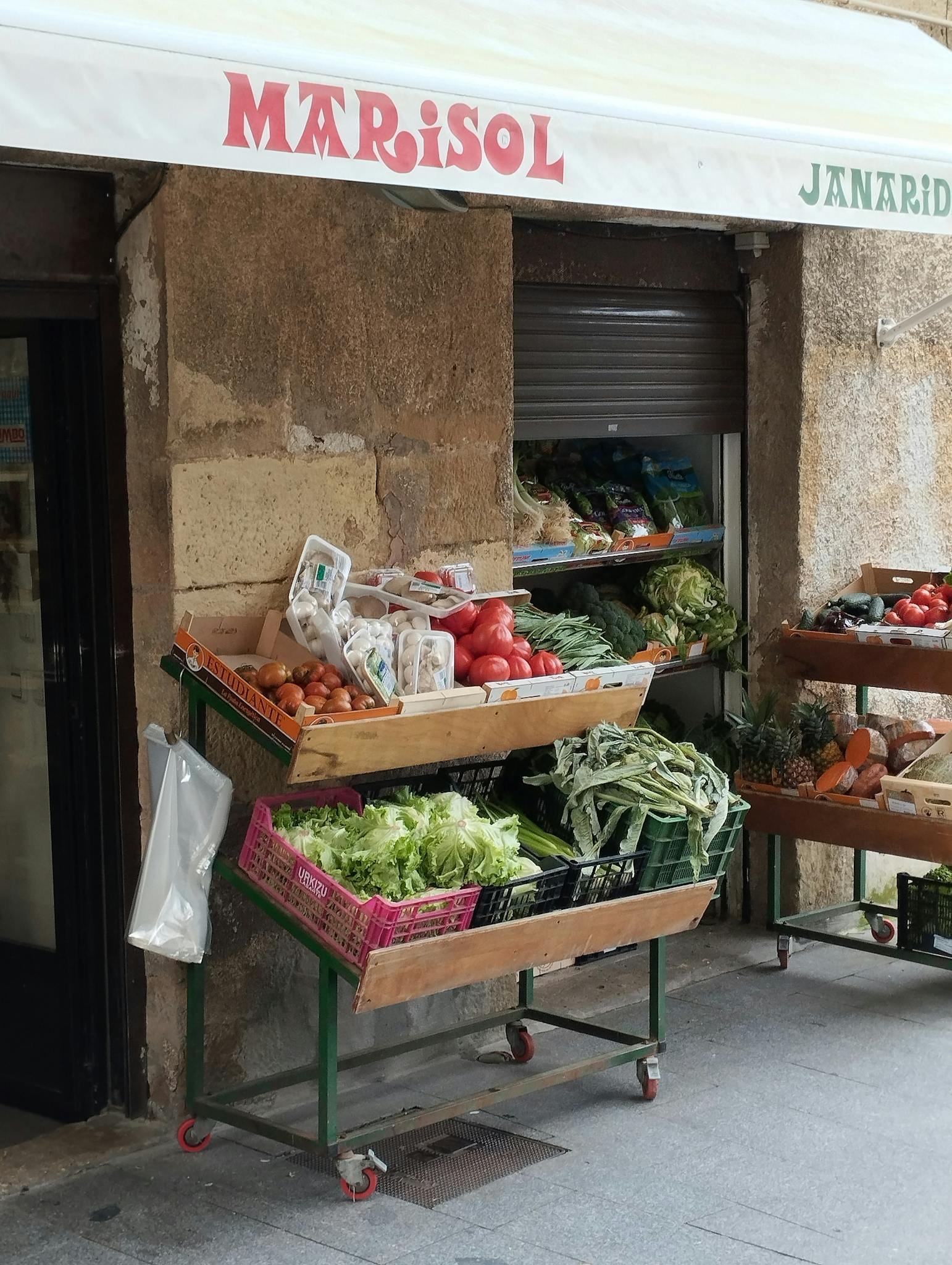 Outdoor market stand displaying fresh vegetables and fruits on a city street.